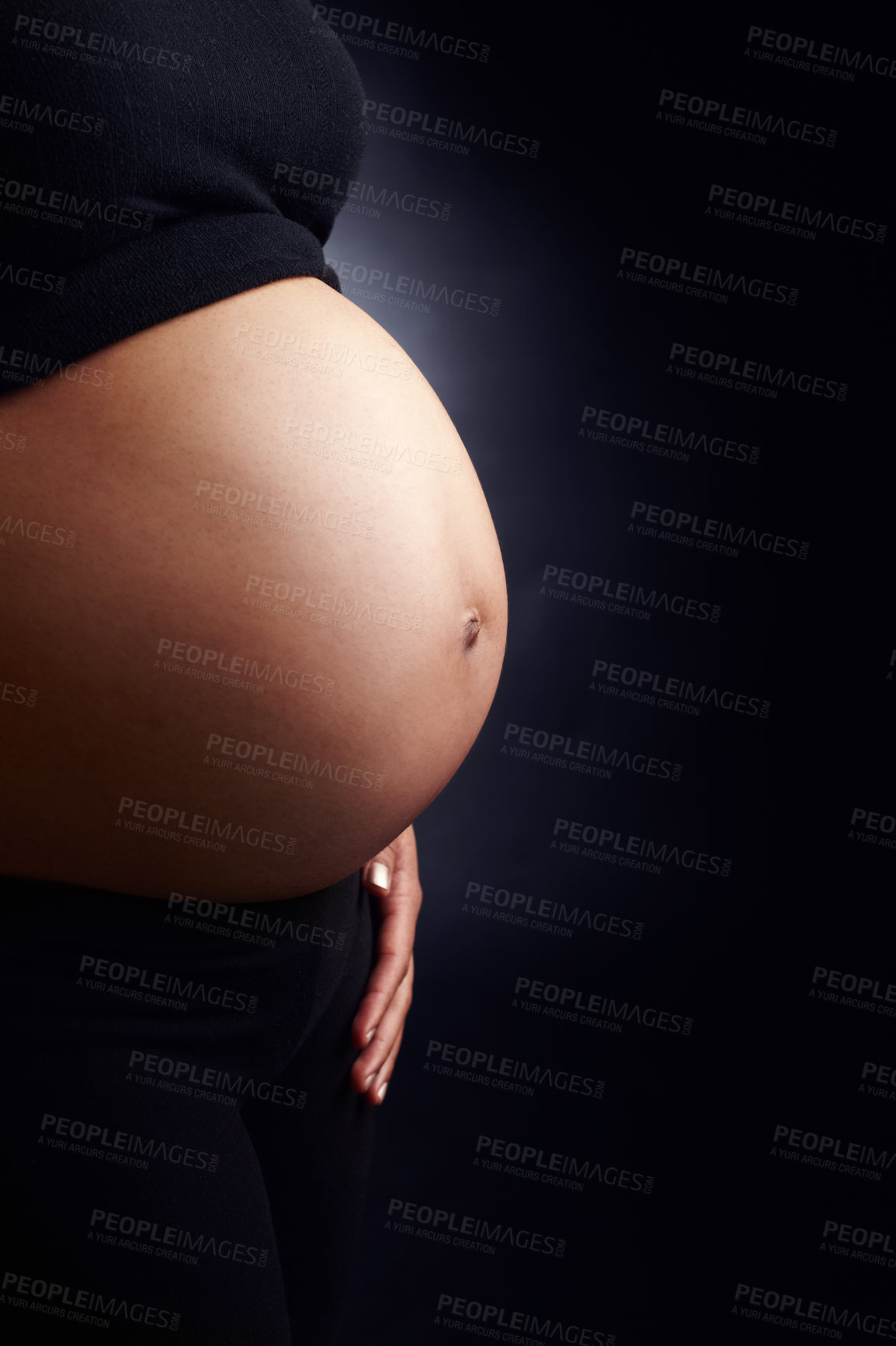 Buy stock photo Closeup of a pregnant woman's bare stomach against a black background. Expecting female showing off her baby bump against a dark studio background. Woman in her last trimester of pregnancy 