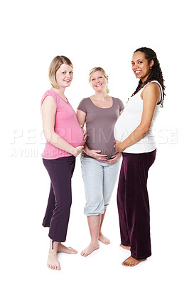 Buy stock photo Three pregnant women smiling broadly at the camera while standing against a white background holding their stomachs