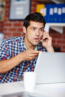 Buy stock photo A shocked young designer taking a call from a client at his desk