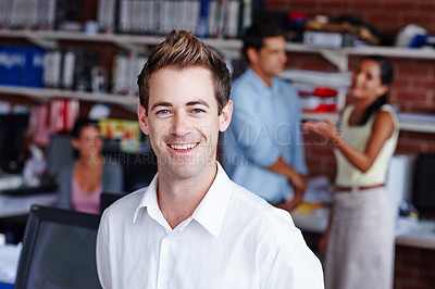 Buy stock photo A handsome young businessman smiling at you while his colleagues work in the background