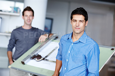 Buy stock photo A handsome young architect standing beside an easel with his blueprint on it