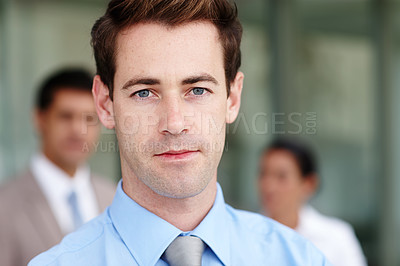 Buy stock photo Closeup portrait of a young businessman with his colleagues blurred in the background