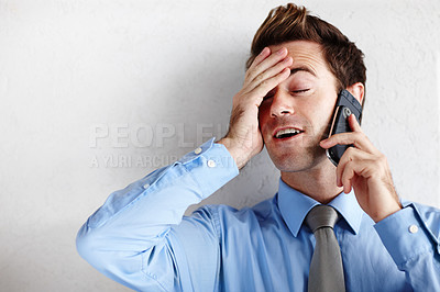 Buy stock photo A relieved young businessman rubbing his face while taking a call