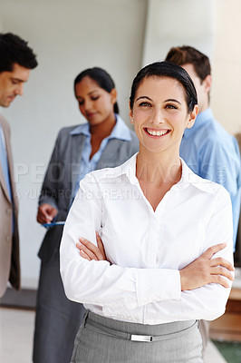Buy stock photo Portrait of a pretty businesswoman crossing her arms while her colleagues converse in the background