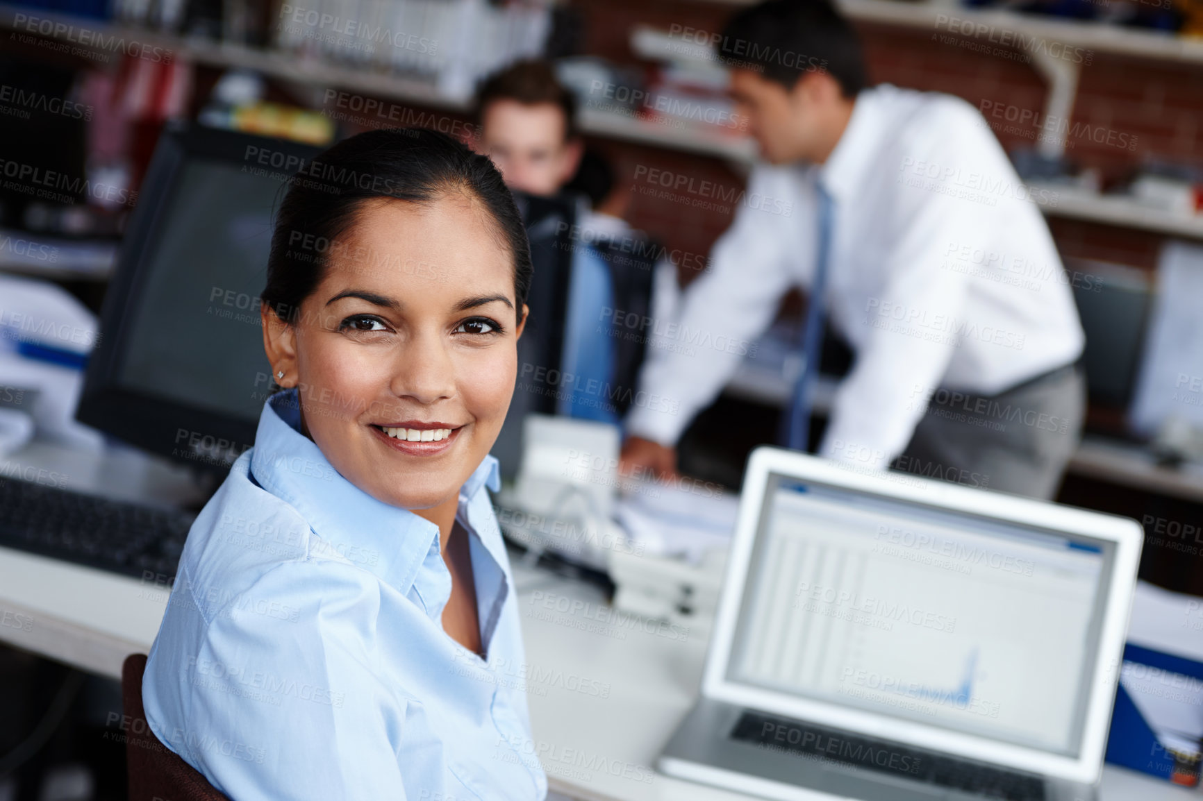 Buy stock photo A pretty young woman glancing over her shoulder while sitting at her workspace