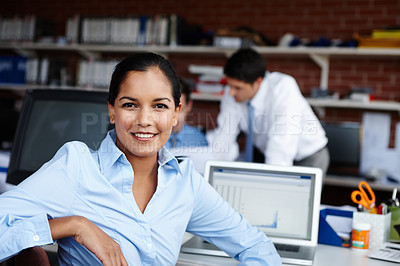 Buy stock photo A pretty young woman glancing over her shoulder at you while sitting at her workspace