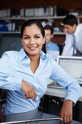 Buy stock photo A pretty young businesswoman turning to look at you while sitting at her workspace