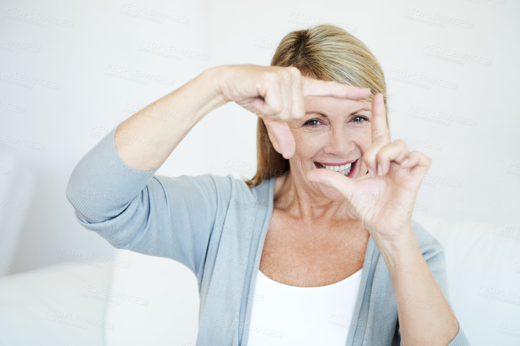 Buy stock photo Portrait of senior woman making frame gesture with her hands sitting on a couch. Smiling older female with great teeth being playful. Creative and fun elderly person using fingers as photography 