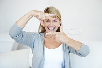 Buy stock photo Portrait of senior woman making frame gesture with her hands sitting on a couch. Smiling older female with great teeth being playful. Creative and fun elderly person using fingers as photography