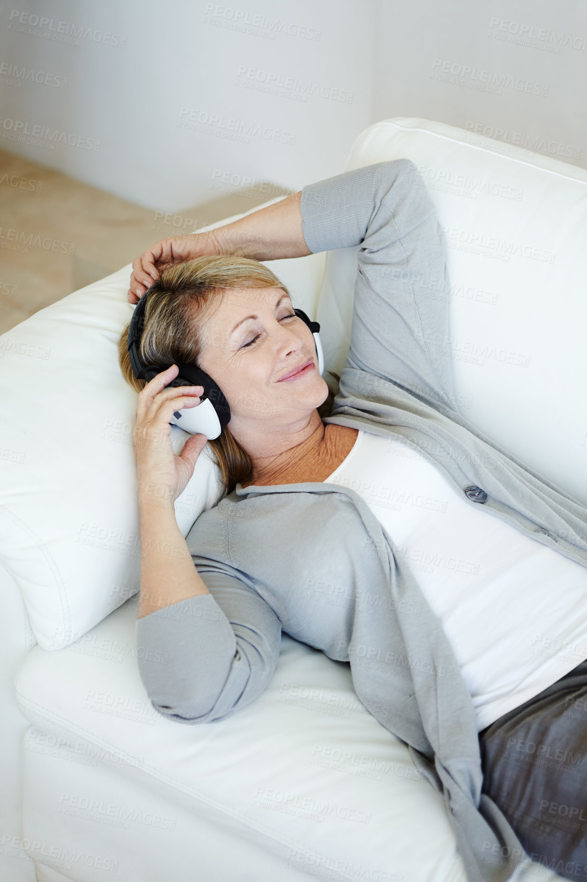 Buy stock photo Woman using headphones listening to music in her lounge. A mature happy female listens to music or a podcast at home relaxing on a sofa alone. Elderly person resting and enjoying retirement at home