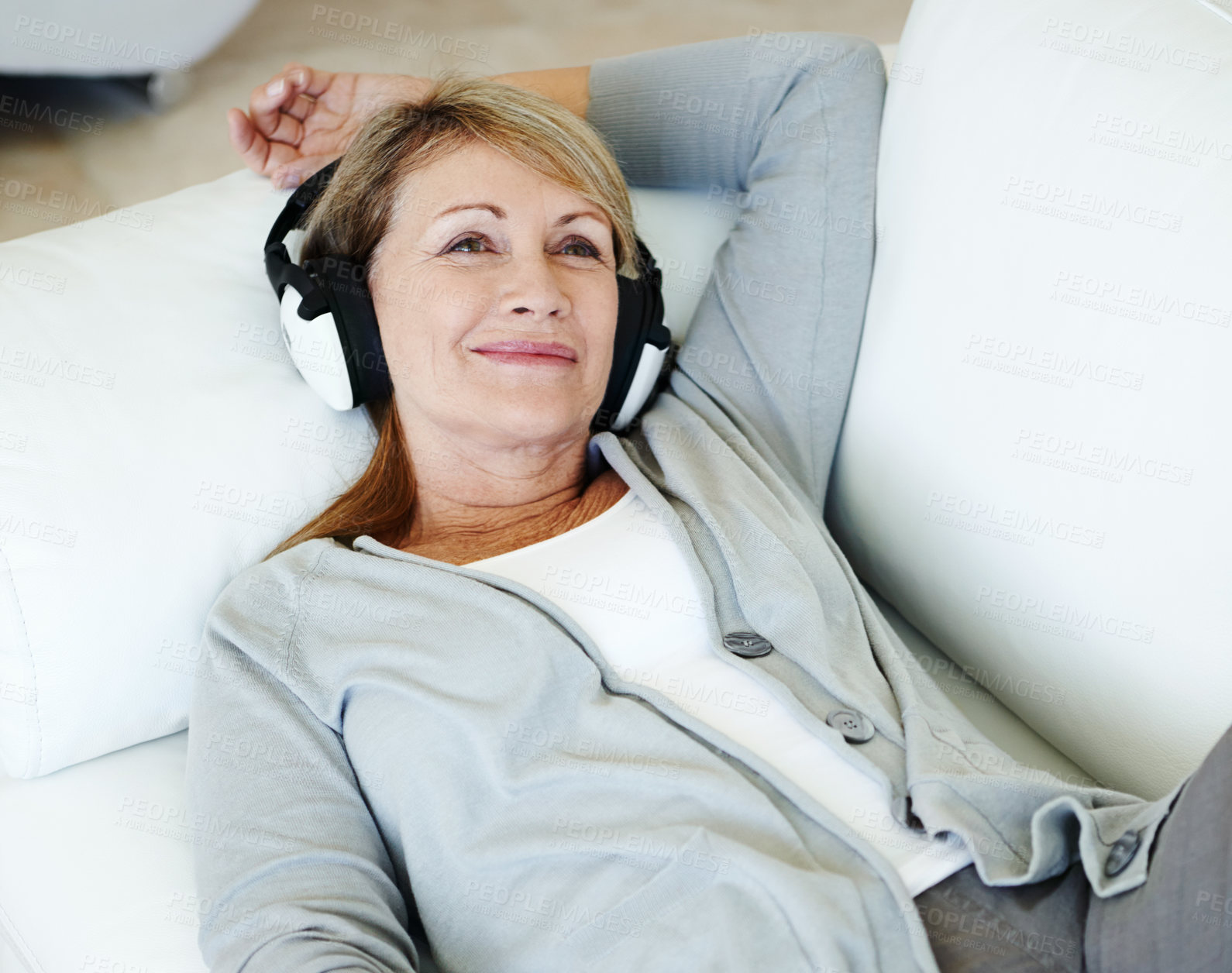 Buy stock photo Senior woman using headphones lying on a couch in her lounge. Older female listening to music or podcast at home relaxing on a sofa alone. Elderly person resting and enjoying retirement in her house