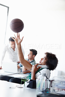Buy stock photo A young man playing with a basketball while sitting in the office