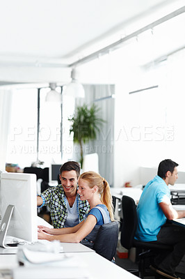 Buy stock photo Two colleagues talking while working on the computer in the office