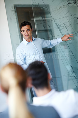 Buy stock photo Attractive casual businessman giving a presentation using a glass window for demonstration