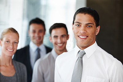 Buy stock photo An african american businessman looking at the camera with his coworkers in the background