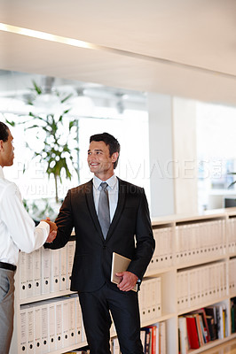 Buy stock photo Two suit-clad businessmen shaking hands while in the office