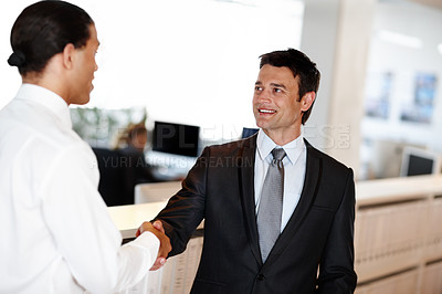 Buy stock photo Two suit-clad businessmen shaking hands while in the office