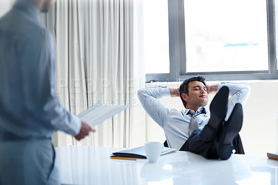 Buy stock photo A laidback businessman with his feet up on his desk as a coworker stands by