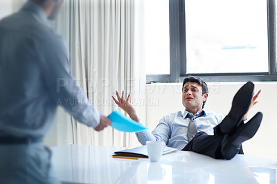Buy stock photo An irritated businessman with his feet up on his desk as a coworker stands by
