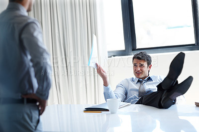 Buy stock photo An irritated businessman with his feet up on his desk as a coworker stands by