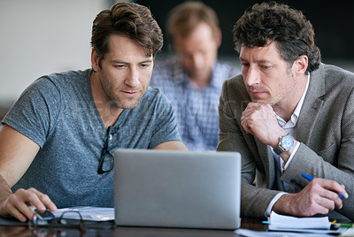 Buy stock photo Cropped shot of two businessmen looking over some work with their colleague in the background