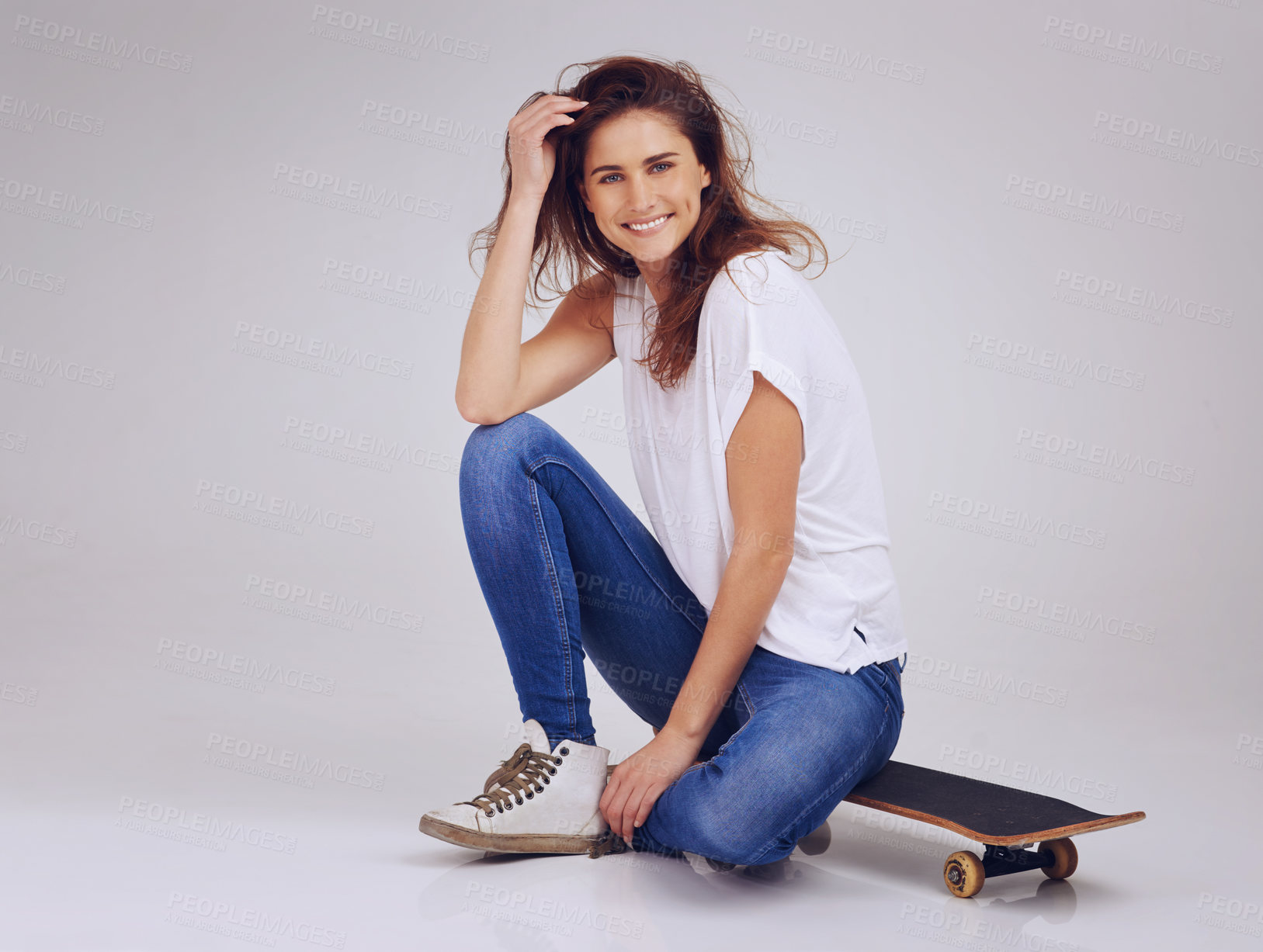 Buy stock photo Studio portrait of an attractive young woman sitting on the floor with a skateboard