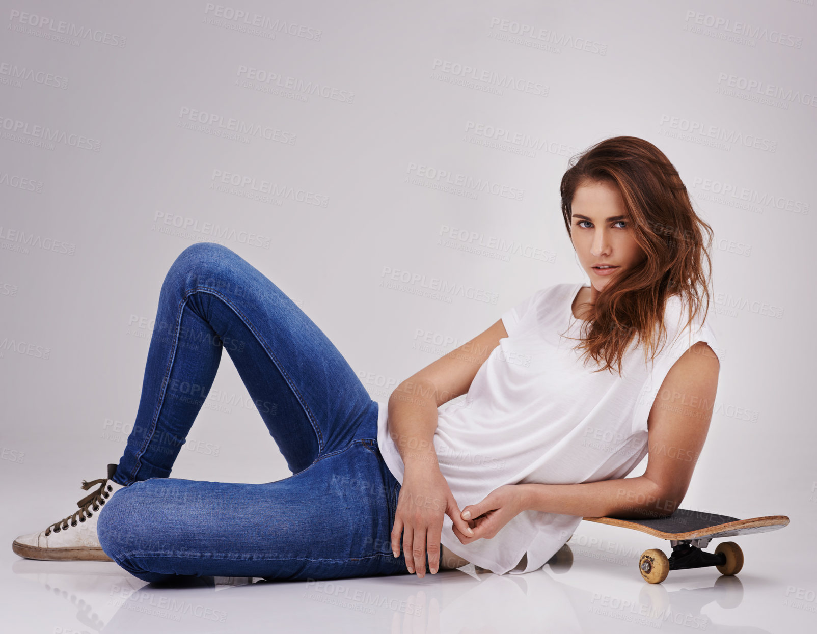 Buy stock photo Studio portrait of an attractive young woman lying on the floor with a skateboard