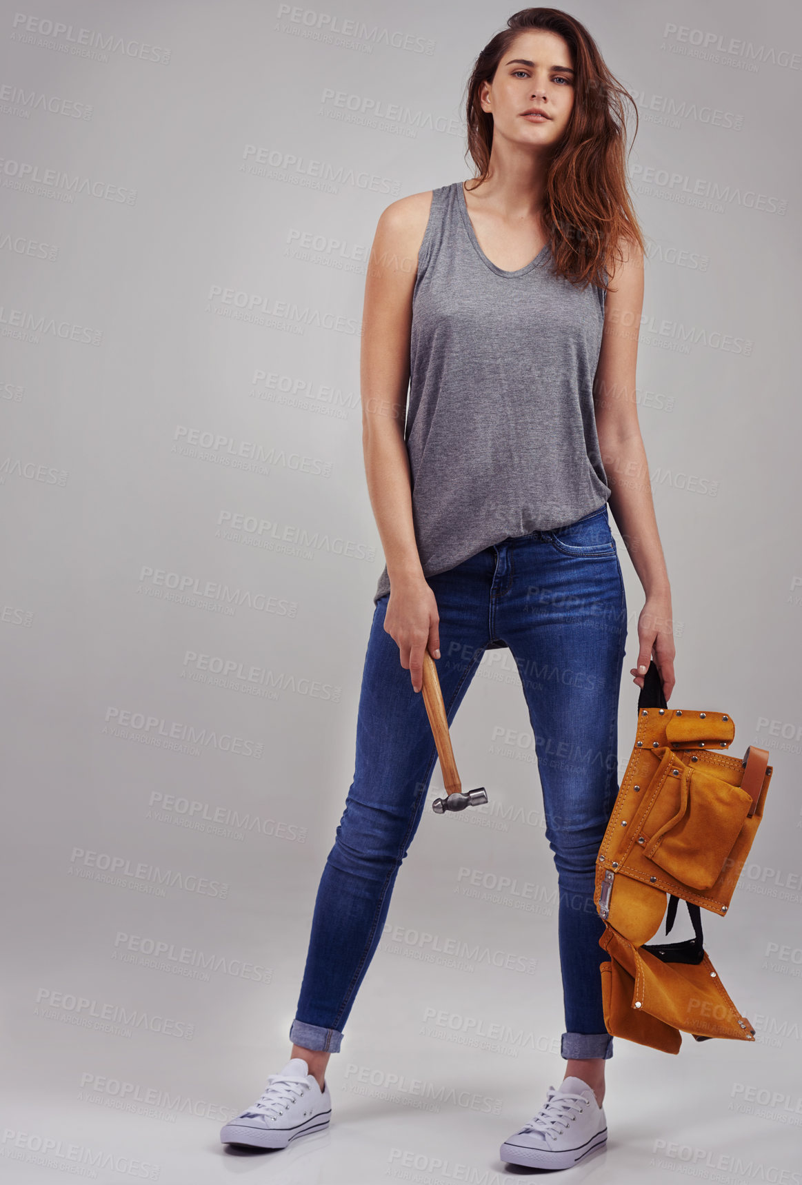 Buy stock photo Full length studio portrait of casually-dressed young woman holding a hammer and tool belt