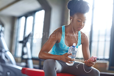 Buy stock photo Phone, headphones and black woman in gym with water for fitness app, workout and subscription. Health, wellness and girl with checking music playlist on smartphone with bottle on break at sports club