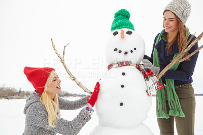 Buy stock photo Shot of two friends building a snowman together