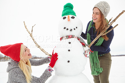 Buy stock photo Shot of two friends building a snowman together