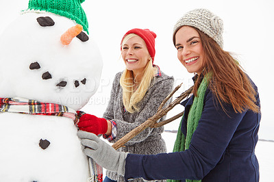 Buy stock photo Cropped shot of two beautiful young women building a snowman