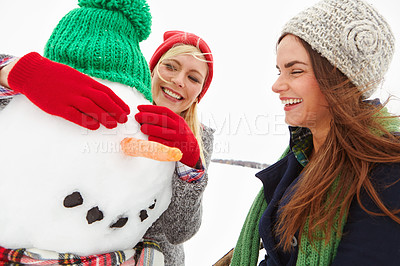 Buy stock photo Cropped shot of two beautiful young women building a snowman