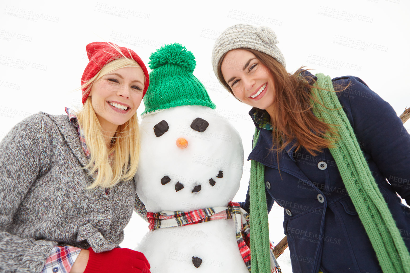 Buy stock photo Cropped shot of two beautiful young women standing beside a snowman
