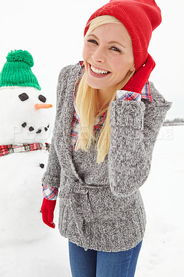 Buy stock photo Three quarter length shot of a beautiful young woman standing infront of a snowman