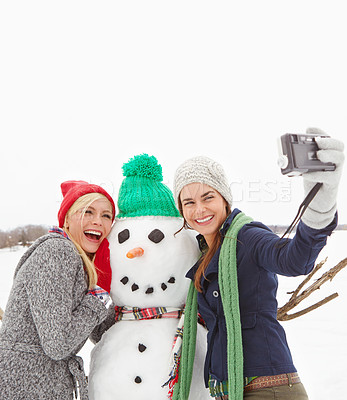 Buy stock photo Cropped shot of two gorgeous young women taking a selfie with a snowman