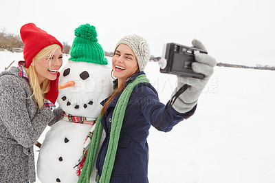 Buy stock photo Cropped shot of two gorgeous young women taking a selfie with a snowman