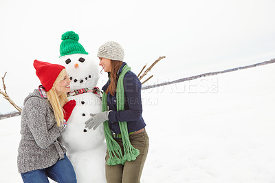 Buy stock photo Cropped shot of two young woman having fun with a snowman