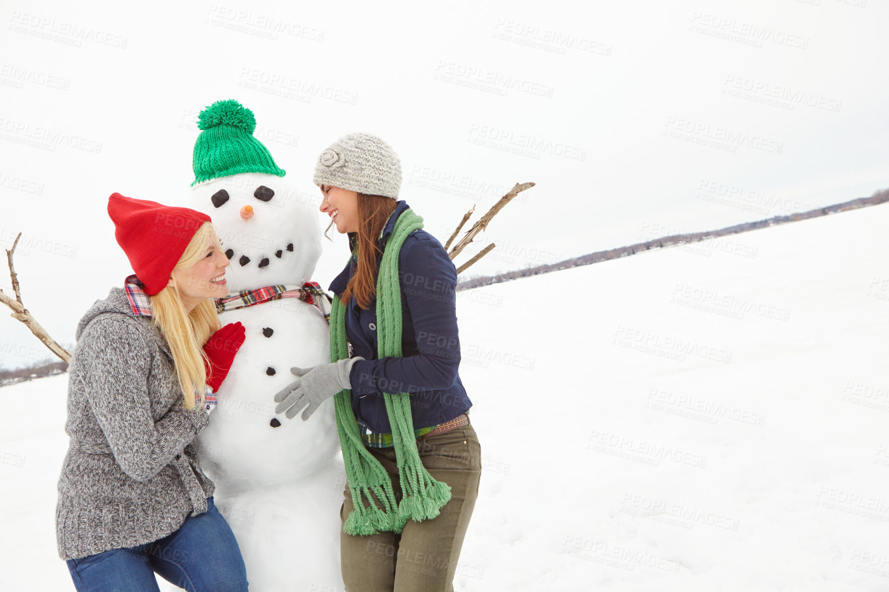 Buy stock photo Cropped shot of two young woman having fun with a snowman