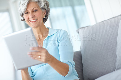 Buy stock photo Shot of a happy senior woman using a digital tablet on the sofa at home