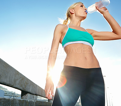 Buy stock photo Low angle shot of an attractive young woman taking a water break while out for a run