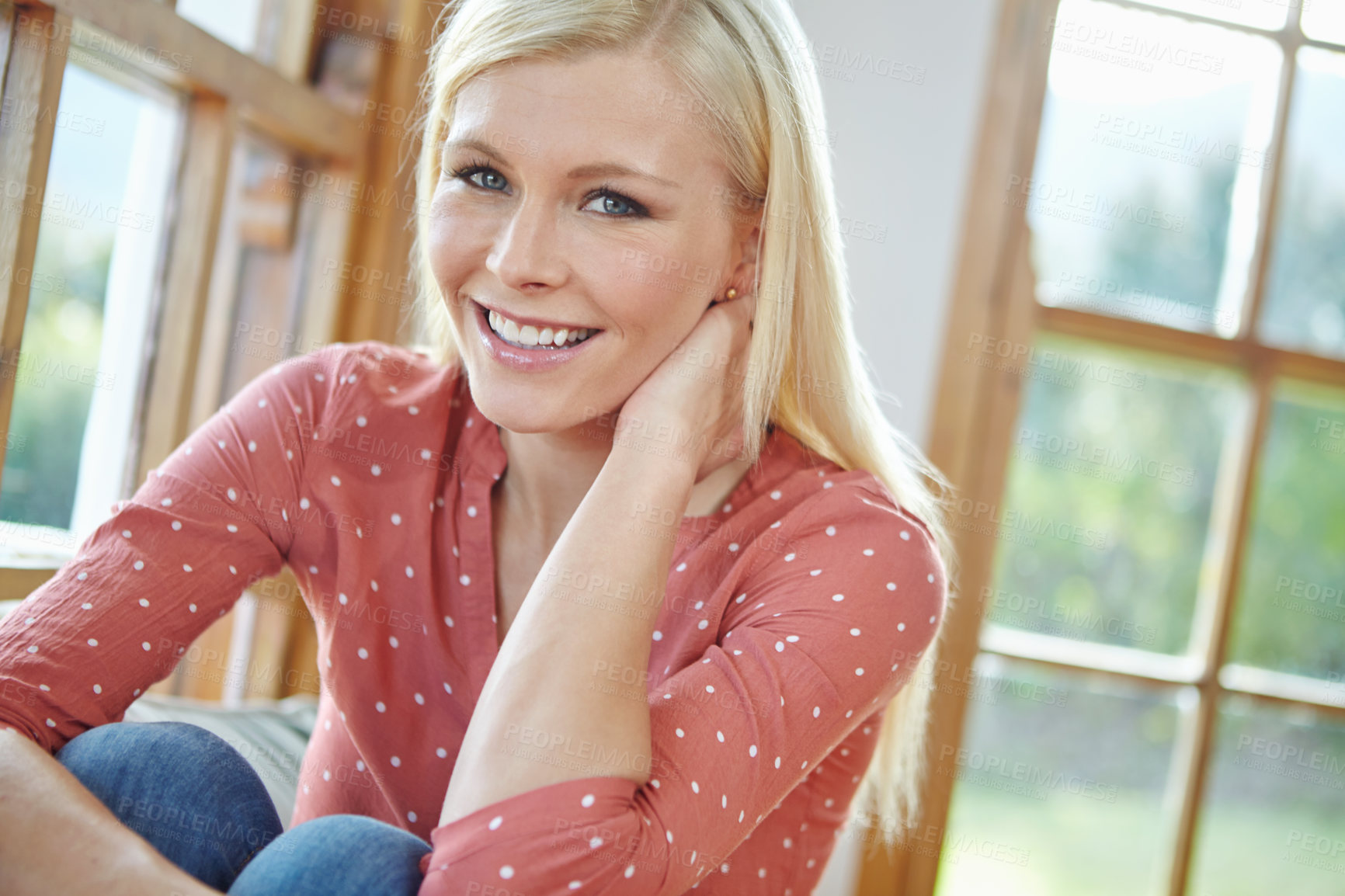 Buy stock photo Portrait of a  beautiful woman smiling and sitting near a window inside a house. Happy attractive blonde woman chilling at home. Happy female relaxing in an apartment enjoying the weekend and me time