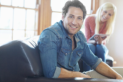 Buy stock photo Portrait of a handsome man relaxing at home on the sofa with his wife sitting next to him