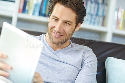 Buy stock photo Shot of a handsome man sitting on the sofa and using a digtal tablet 