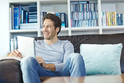 Buy stock photo Shot of a handsome man sitting on the sofa and using a digtal tablet 