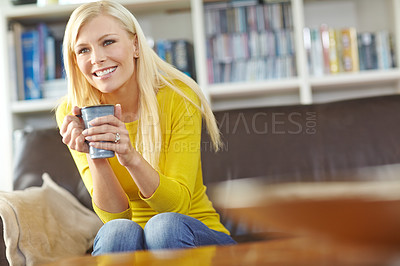 Buy stock photo A beautiful woman smiling and sitting on her living room sofa at home. Happy attractive blonde woman chilling drinking coffee. Happy female relaxing and daydreaming at home and enjoying her free time