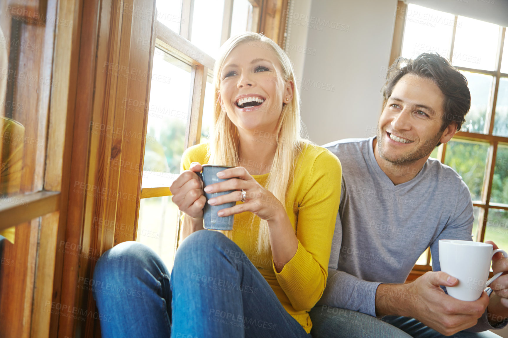 Buy stock photo Shot of a happy couple enjoying a hot drink together next to a window at home