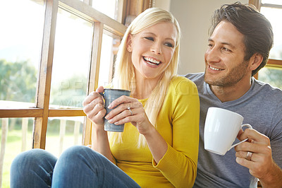 Buy stock photo Shot of a happy couple enjoying a hot drink together next to a window at home