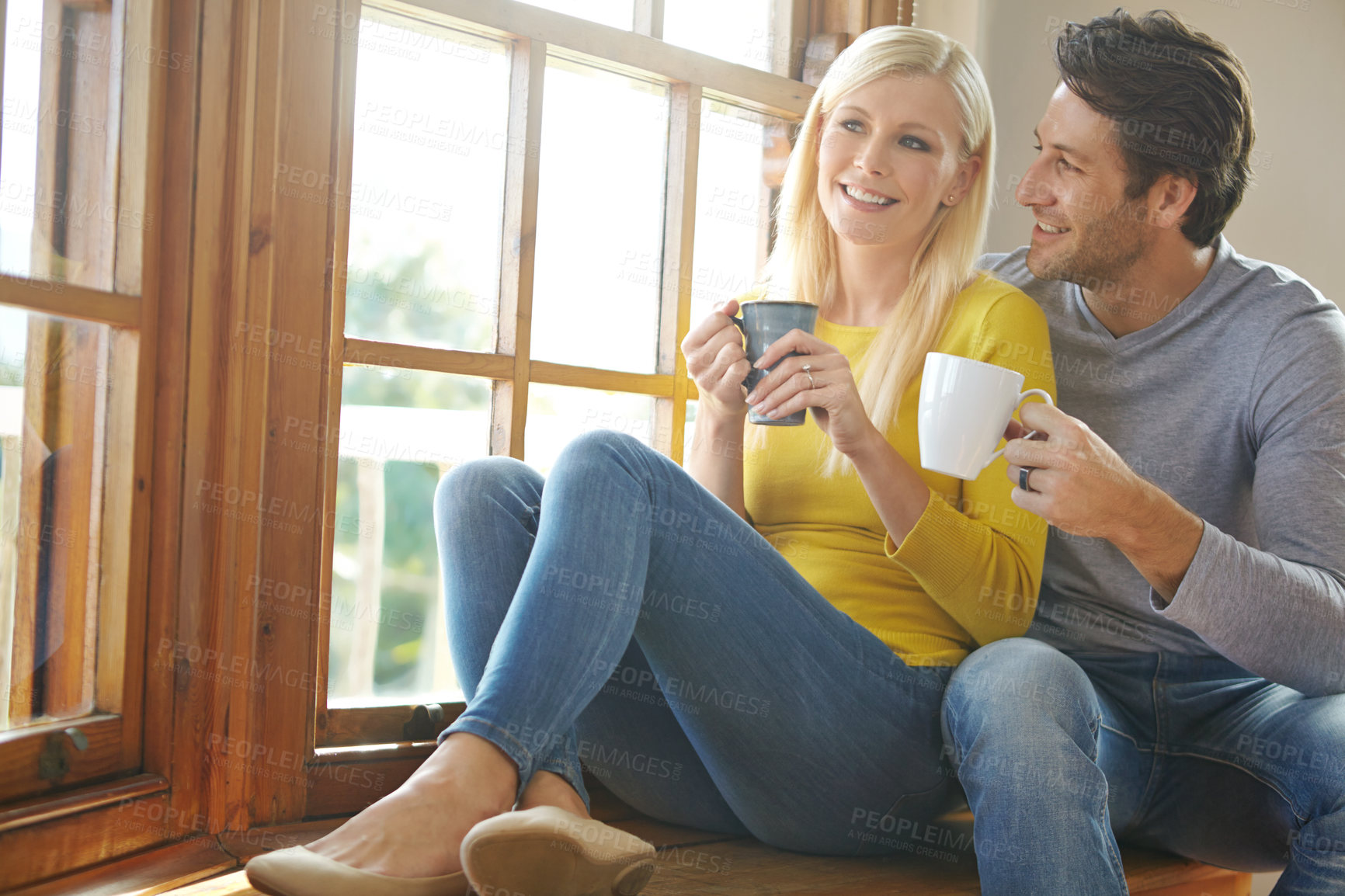 Buy stock photo Happy couple, relax and window with coffee for bonding, morning or holiday weekend together at home. Young man and woman with smile, beverage or drink for friendly discussion or conversation at house