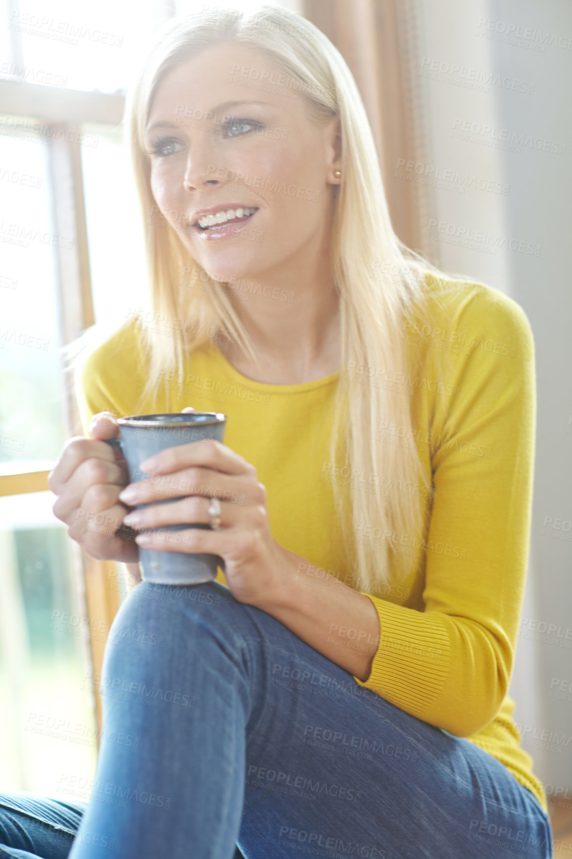 Buy stock photo A beautiful woman smiling and sitting near a window inside a house. Happy attractive blonde woman chilling drinking coffee. Happy female relaxing and daydreaming at home off the grid in a sunroom